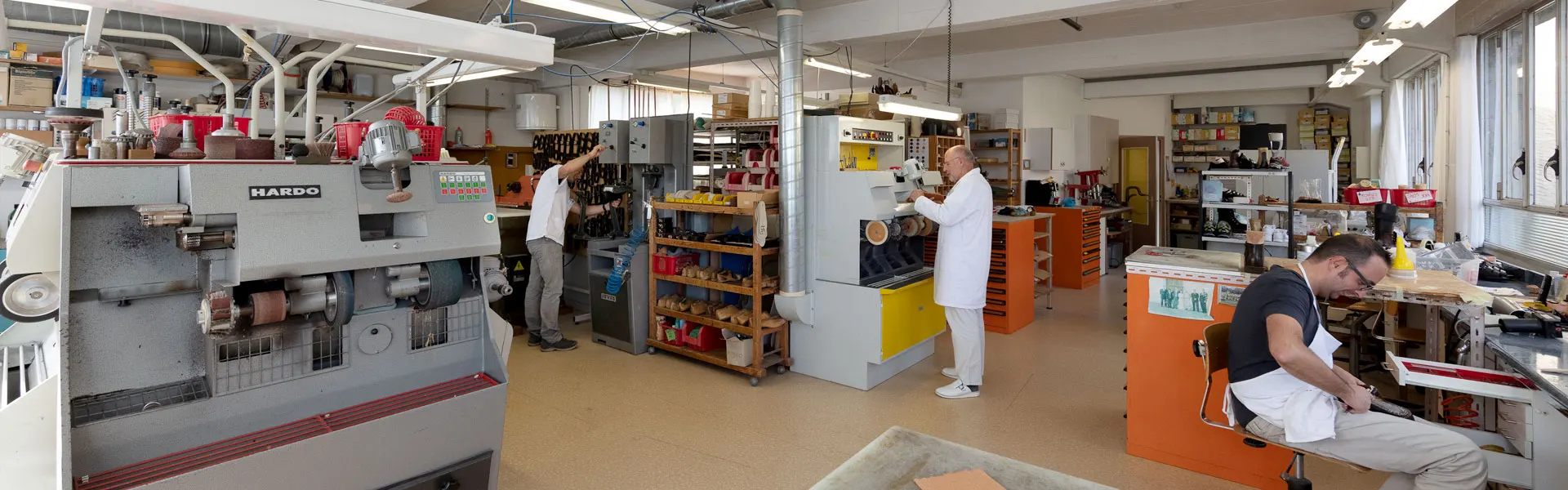 Il laboratorio di Muralto: macchine per la lavorazione, scaffali con le forme in legno, tre persone al lavoro