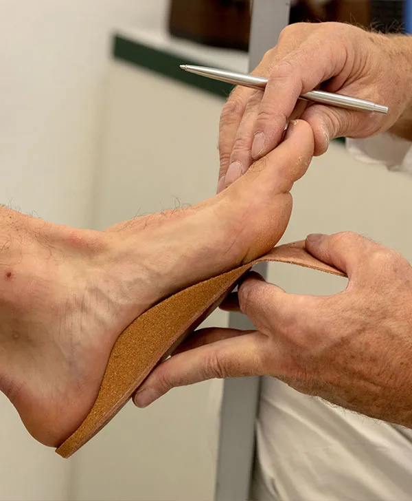 Le mani del tecnico provano un plantare in sughero sotto il piede del paziente