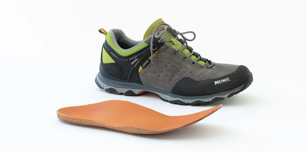 Una scarpa da escursione Meindl accanto a un plantare in pelle e sughero